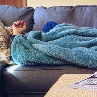 Person with blanket over their head lying on the couch.