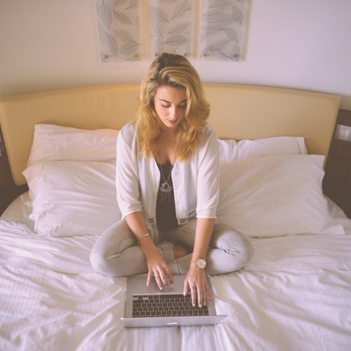 Woman sitting on her bed using a laptop.