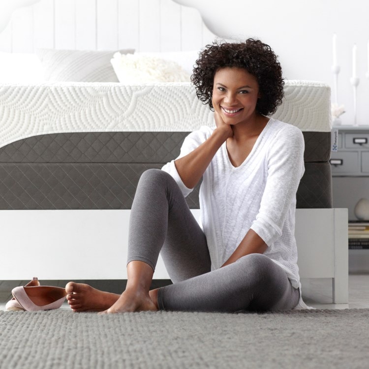 Woman sitting in front of her bed.