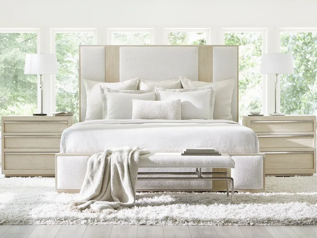 king upholstered bed with two light wood nightstands and an upholstered accent bench