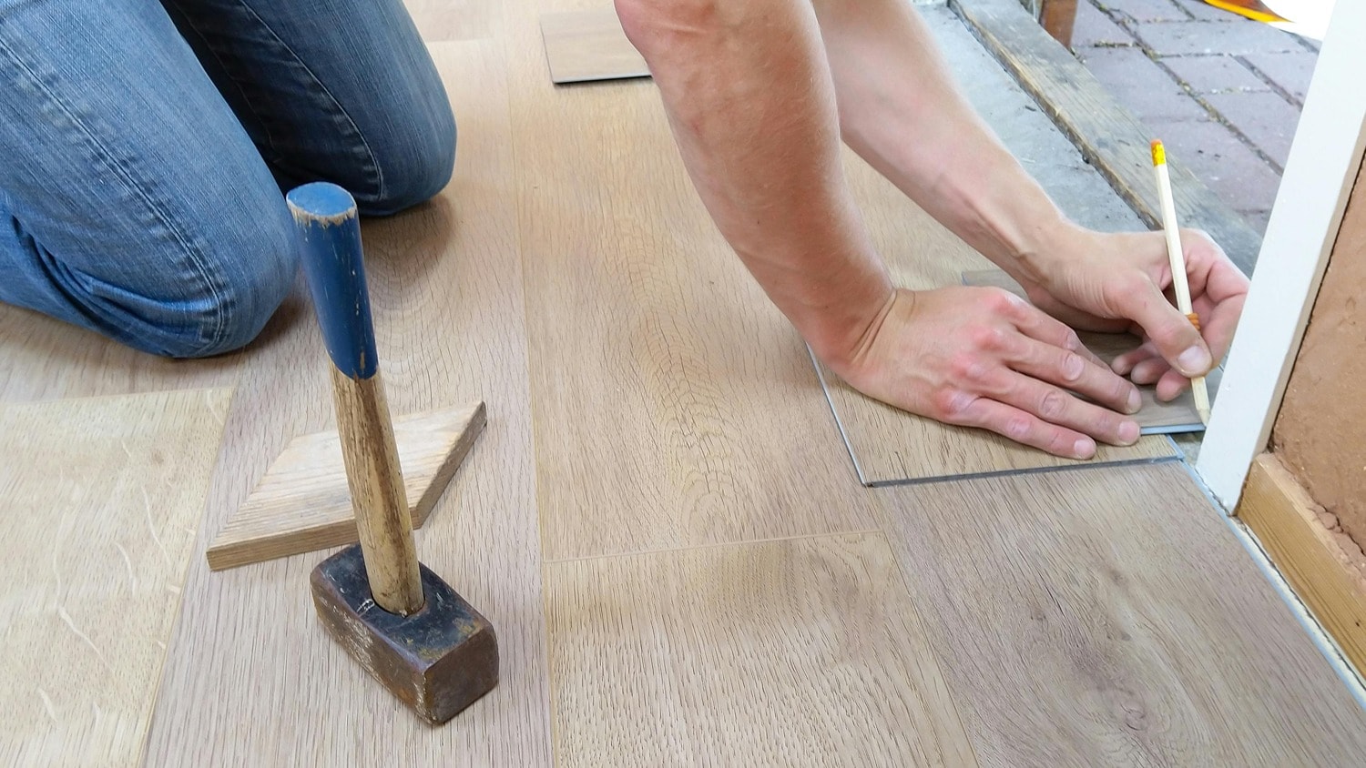 mens hands laying down light wood toned hardwood flooring