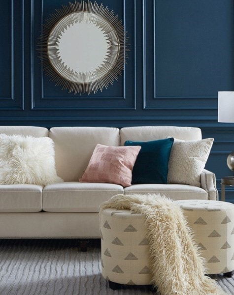 white sofa with multicolored pillows, ottoman and blanket in a room with blue walls