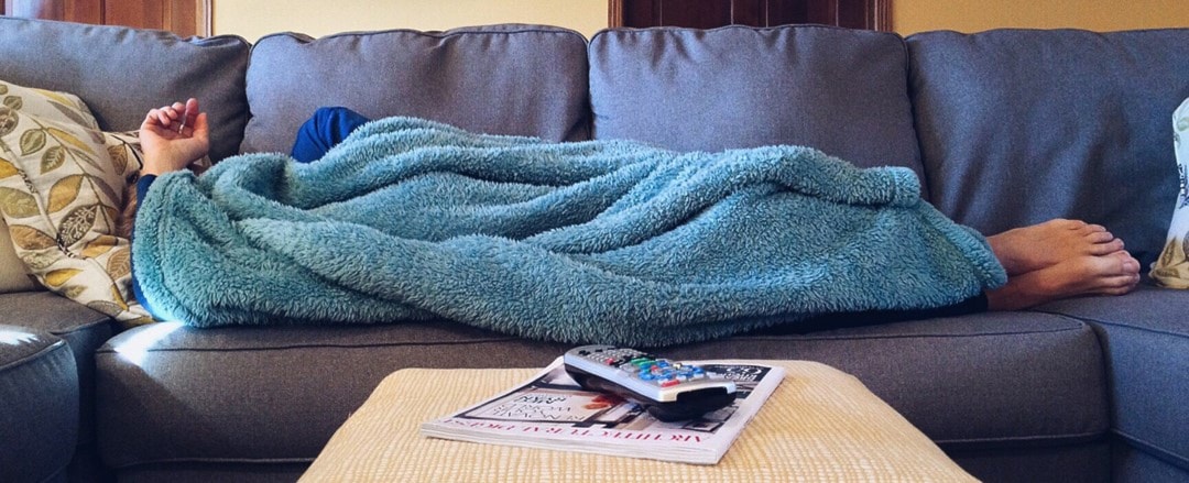 person laying on sofa wrapped in blue blanket