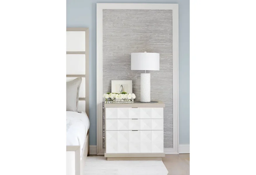 White, clean three-drawer night stand with textured surface next to a bed. 