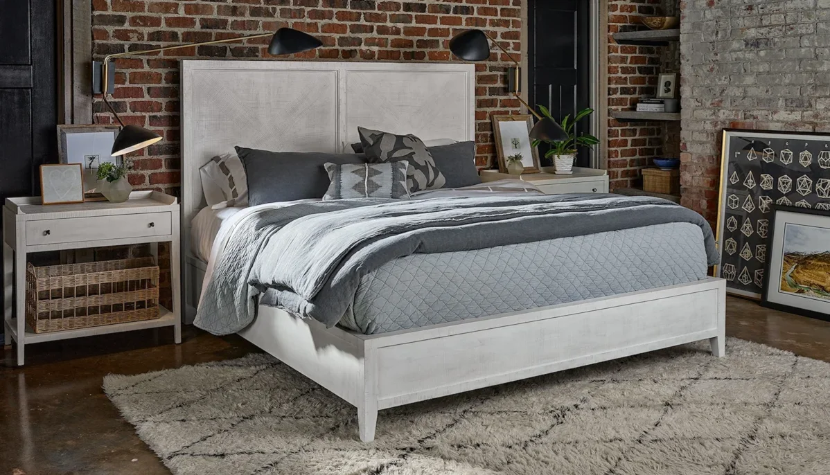 Beautiful white-washed wood frame bed in a modern farmhouse bedroom with exposed brick walls. 