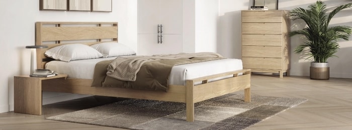 Bedroom set with wooden bed, nightstand and chest of drawers with white bedding and a rug. 